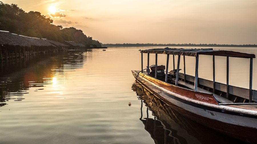 Wooden boat with a canopy moored on calm water at sunset near Siem Reap, Cambodia